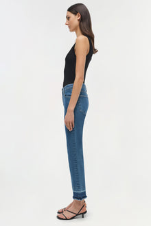 Woman wearing black sleeveless tank top and blue straight-leg jeans with frayed ankle hem, shown in side profile.