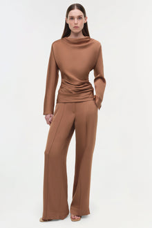 Camel-brown satin top with cowl neckline and ruched side detail, long sleeves, worn with matching wide-leg trousers.