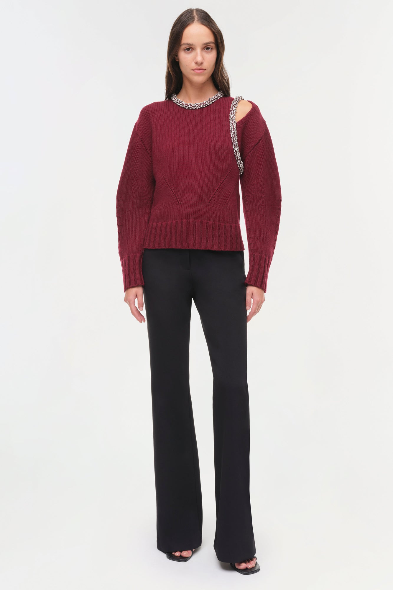 Burgundy ribbed pullover with beaded neckline and shoulder cutout, paired with black flared pants.
