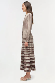 Woman wearing a brown and cream ribbed knit cardigan with geometric patterned skirt, shown from the side.