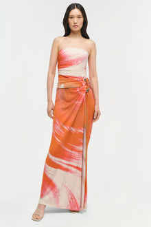 Strapless jersey gown with pink and orange ombre brushstroke print, ruched waist, and asymmetrical draped skirt.