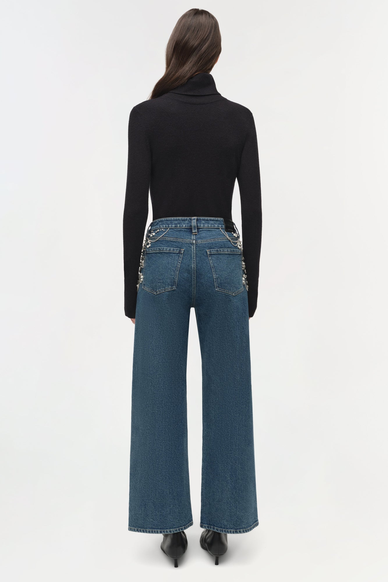 Blue denim crop jeans with embellished pocket details, worn with black turtleneck and heels.