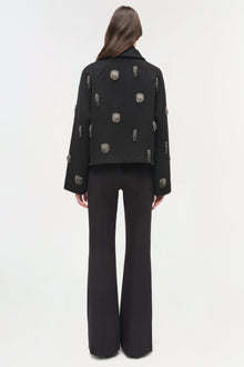 Black cropped jacket with silver beaded embellishments scattered across back and sleeves, worn with black flared trousers.