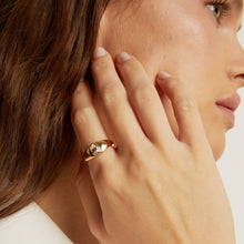 Model. Close-up of a woman wearing a gold ring on her hand, with a neutral background.
