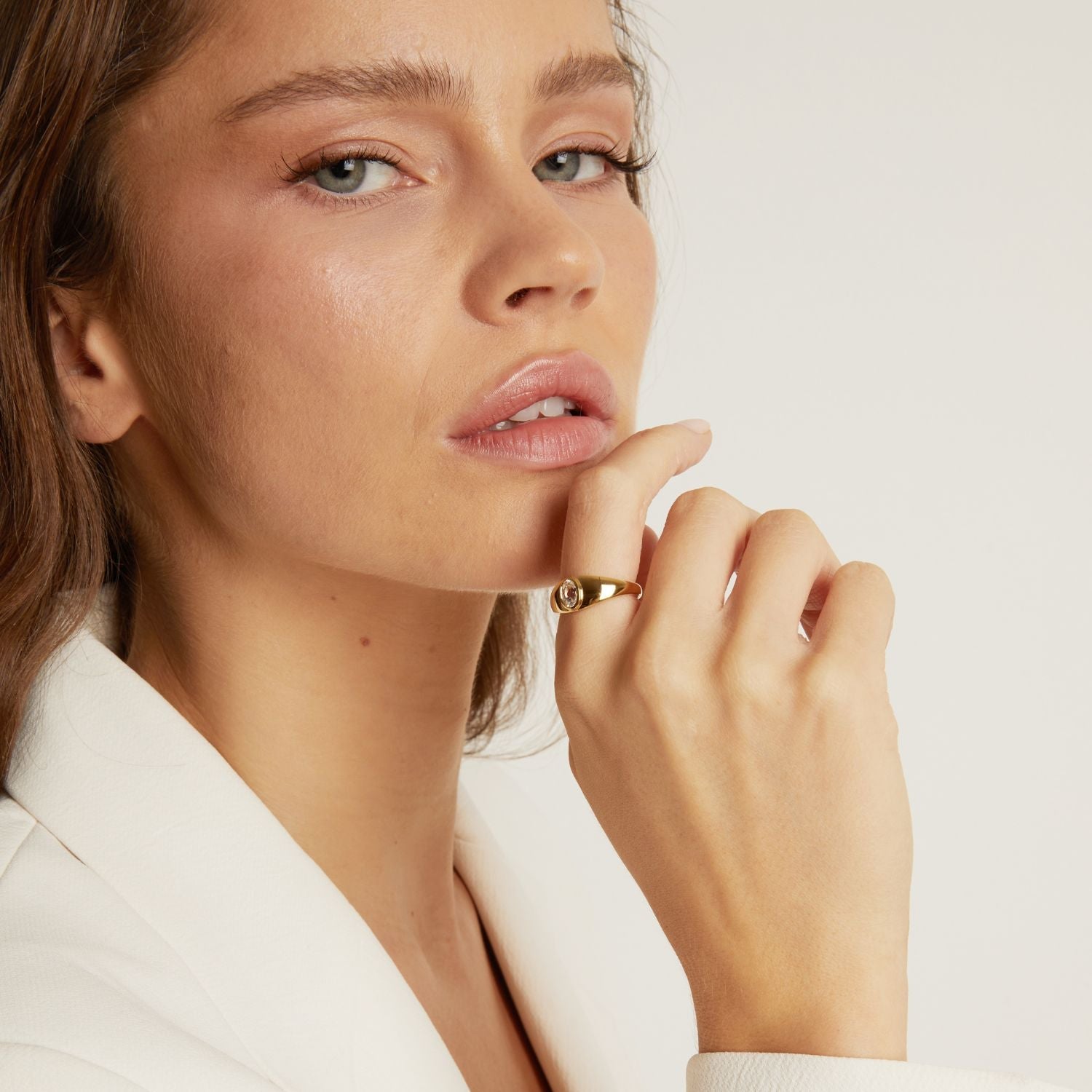 Model. Close-up of a woman wearing a gold ring on a plain background