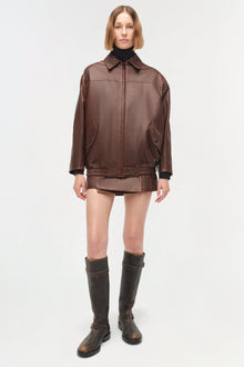 Brown leather jacket with collar, front zip, hand pockets, and ribbed cuffs worn over black turtleneck and matching skirt.