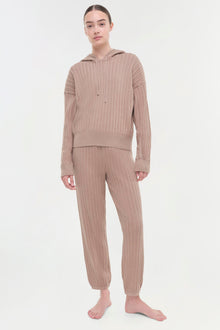 Beige cable knit hoodie and matching pants set on model against white background.