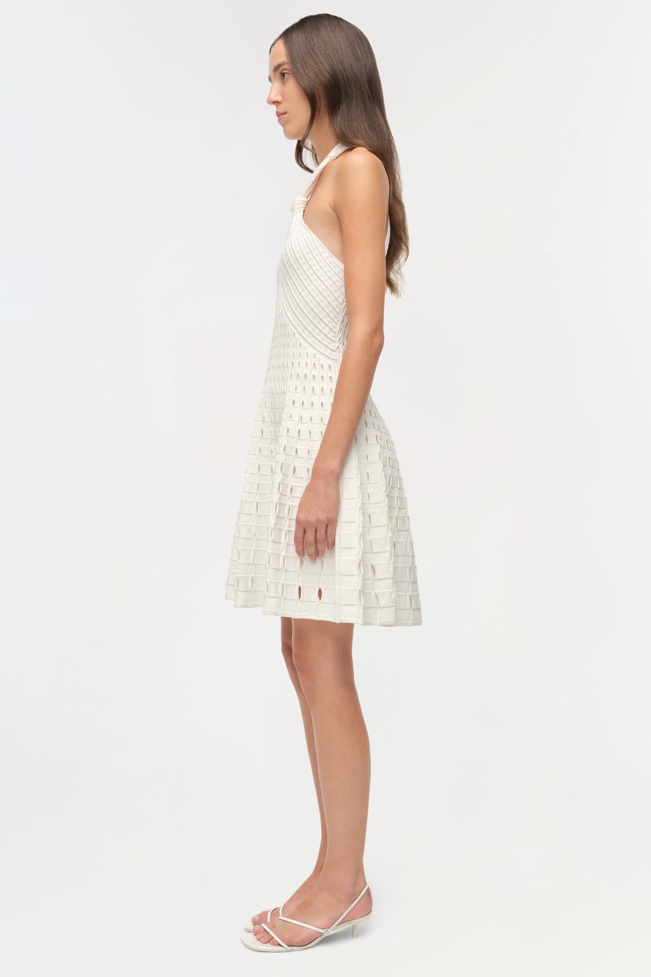White sleeveless knit mini dress with eyelet pattern throughout, shown on model in side profile view.