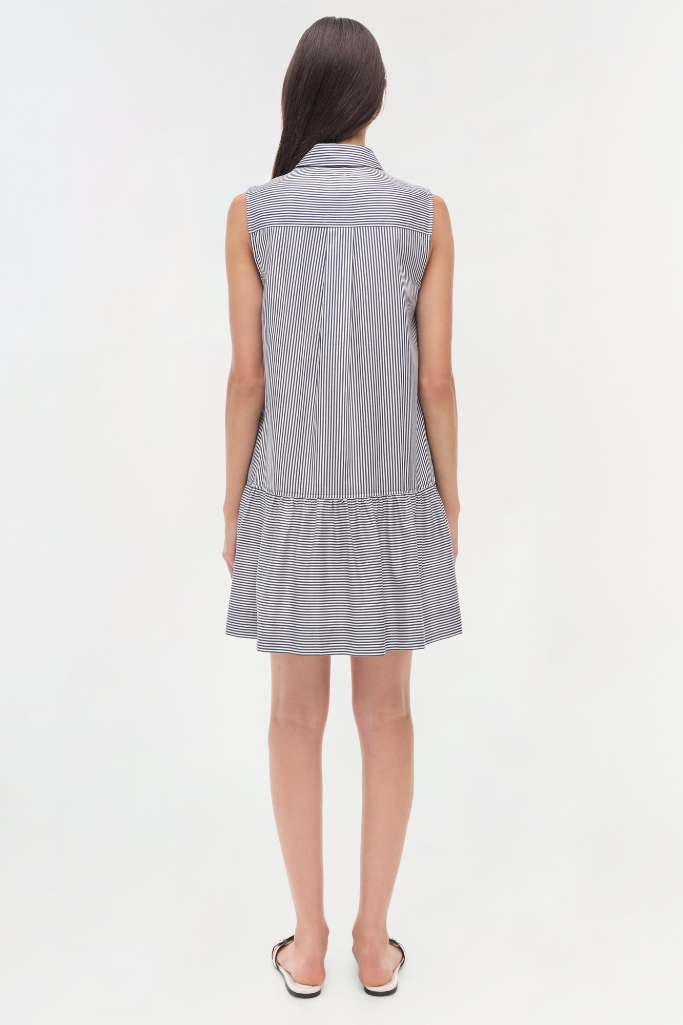 Woman wearing a sleeveless blue and white striped shirt dress with a collared neckline and dropped waist.