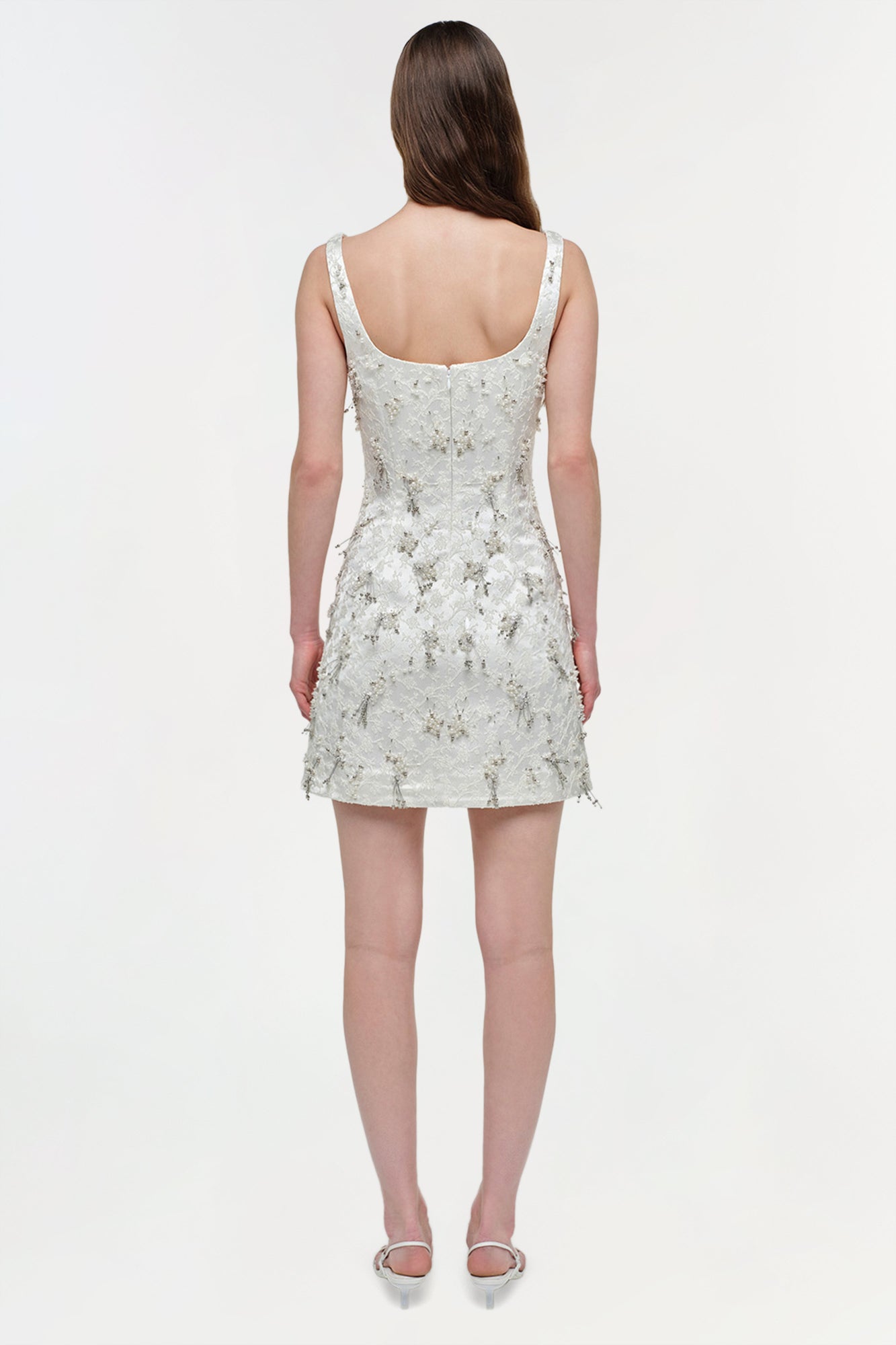 White sleeveless mini dress with all-over beaded embellishment, scoop neckline, and fitted bodice, shown on model from back.