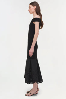 Woman wearing black off-shoulder knit midi dress with embroidered lace hem detail.