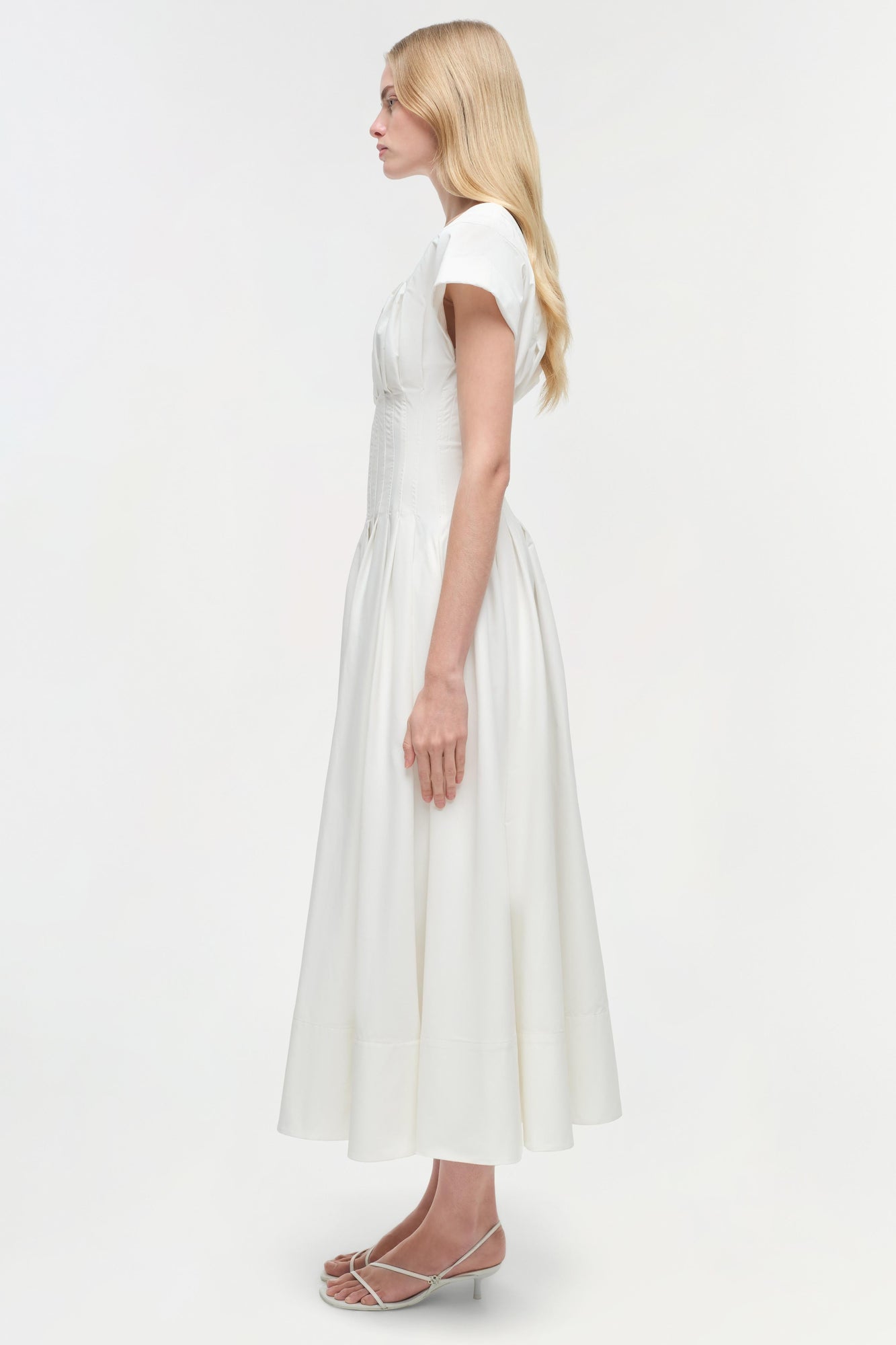 Woman wearing white cotton midi dress with short sleeves and full skirt, shown from the side.
