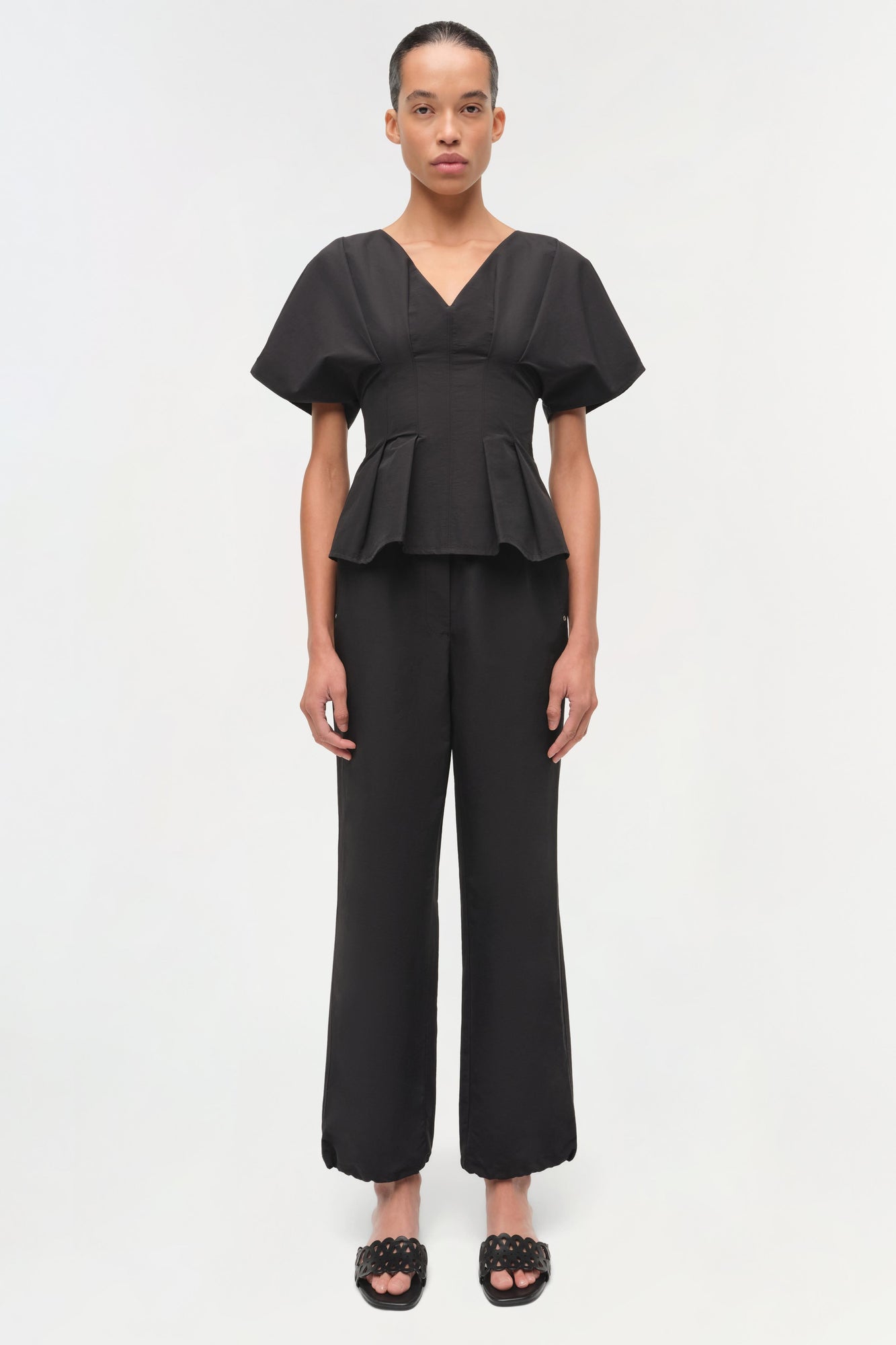 Black cotton faille top with V-neckline, short puffed sleeves, and peplum waist detail.