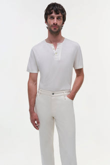 Man wearing cream-colored wide leg jeans with a white short-sleeve henley shirt.