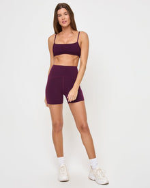 Front view of the LSPACE En Pointe Short in plum on a model against a white background, showing the high-waist active shorts, paired with the matching plum Stride Bra.
