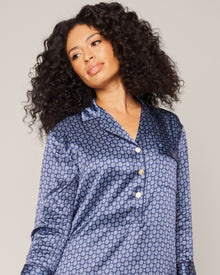 A person with long, curly hair wearing a Petite Plume Womens Silk Nightshirt in Midnight Foulard and a stylish neck scarf stands against a plain background, looking slightly to the side.