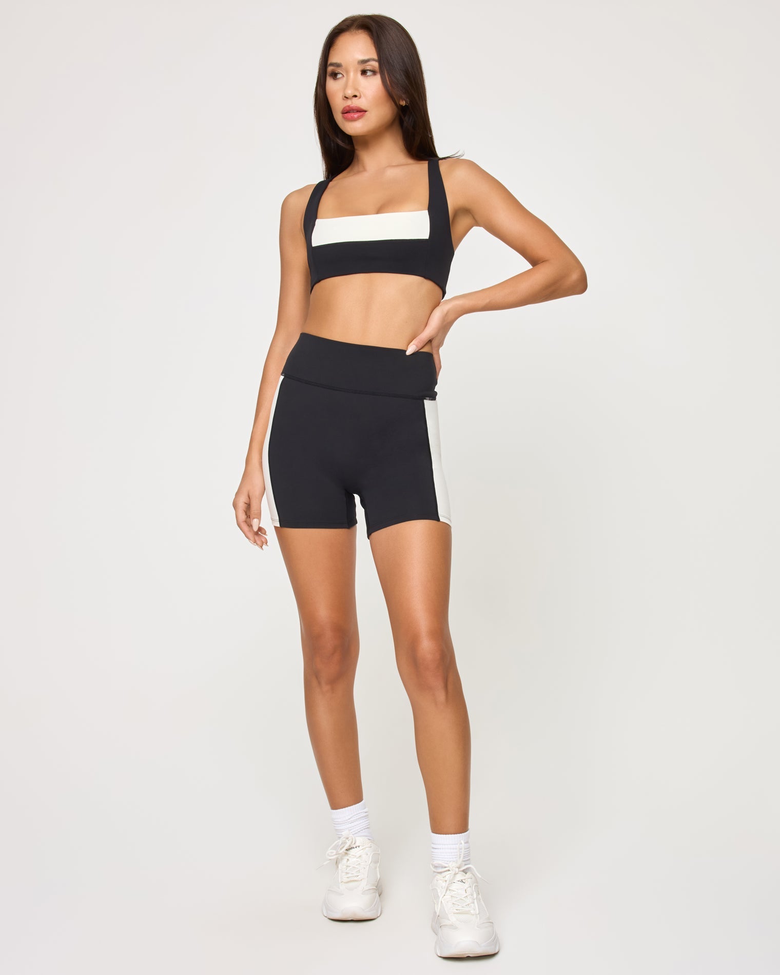 Front view of the LSPACE Uppercut Bra in black-cream on a model against a white background, showing the square-neck sports bra with cream trim, paired with matching black-cream high-rise active shorts.