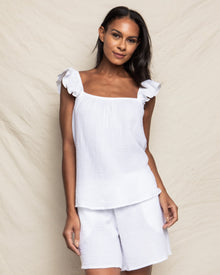 A person wears the Womens Gauze Celeste Top in White by Petite Plume, featuring ruffled shoulders and matching shorts, standing against a neutral background with a confident smile.