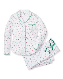 Petite Plumes Womens Flannel Pajama Set in Apres Ski features white pajamas adorned with holiday-themed red and green skiers. Made from brushed cotton flannel, it includes a long-sleeve button-up top with a chest pocket and matching pants with an elastic waistband, highlighted by green piping edges.
