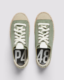 P448 green canvas sneaker with white rope laces and tan recycled suede heel tab, showcasing the organic jute sole and amber rubber tread from a front angle.