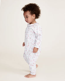 The Baby's Twill Madeline Romper in Love Song is a white long-sleeve romper with ruffled cuffs and collar, decorated with a pink pattern of hearts, glasses, and small animals. It features snap buttons down the front and legs.