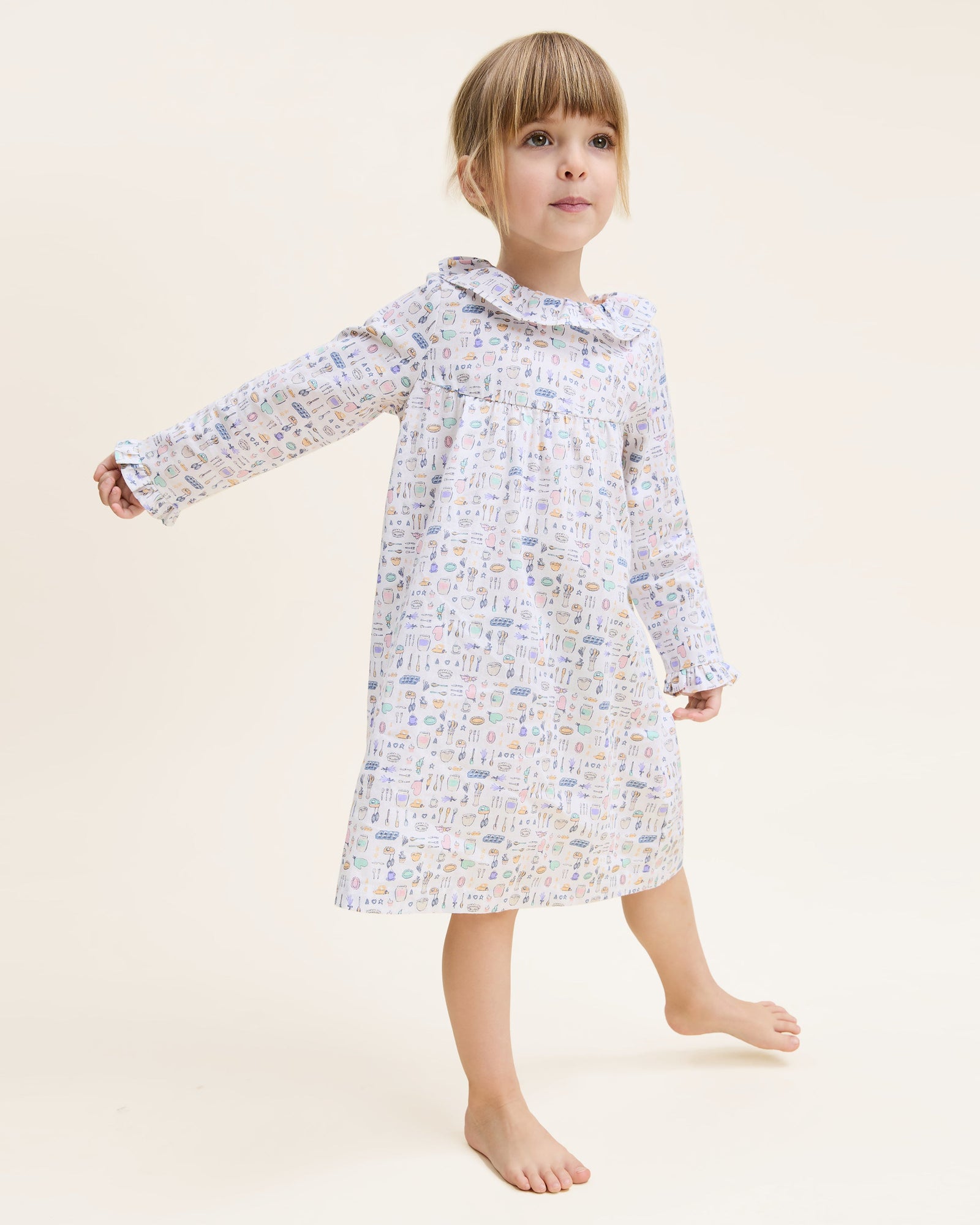 The Kid's Twill Scarlett Nightgown in Baking Spirits Bright features long sleeves, a ruffled collar and cuffs, and a pastel cupcake, teapot, and cutlery print on a white background.