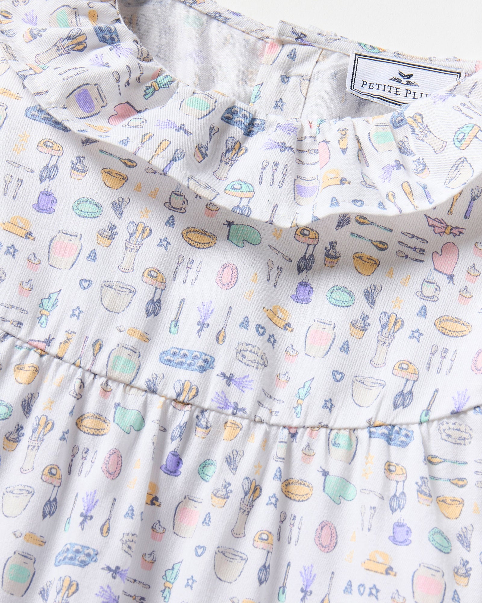 The Kid's Twill Scarlett Nightgown in Baking Spirits Bright features long sleeves, a ruffled collar and cuffs, and a pastel cupcake, teapot, and cutlery print on a white background.