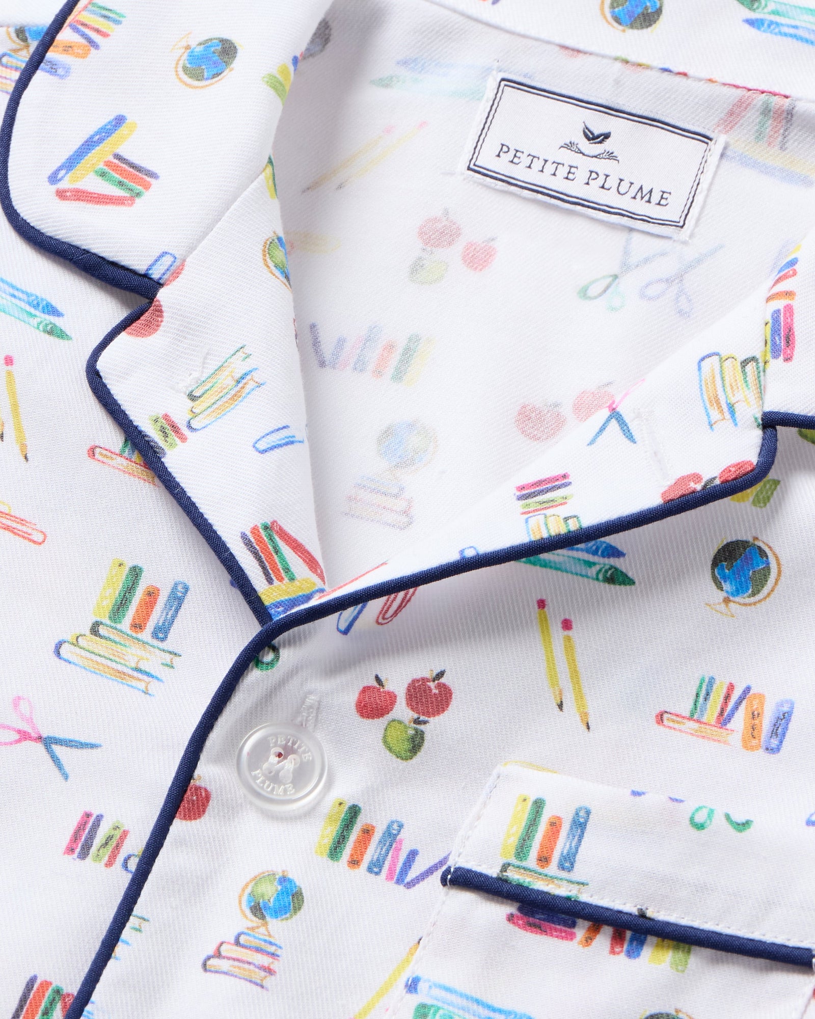 The Kid's Twill Short Set in Literary Lessons features a white base with colorful school-themed prints—pencils, books, and erasers—plus navy piping on the collar, pocket, sleeves, and shorts.