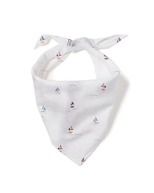 A fluffy white dog sits on the wooden floor, joyfully grinning with its tongue out, wearing a Dog Twill Bandana in Bateau by Petite Plume—perfectly showcasing stylish dog accessories.