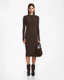 A woman faces forward, wearing the Rudsak AGNES - 8524551 Espresso fitted bodycon dress with long sleeves, paired with brown ankle boots and a brown handbag against a plain white background.