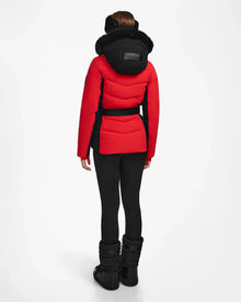 A person stands facing away, wearing the Rudsak ALAIA - 8124816 Flame Red ski jacket with a black belt, paired with black leggings and winter boots against a plain white background.