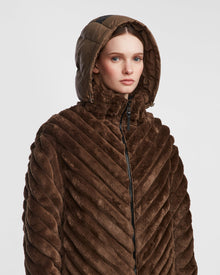 A woman wearing the Rudsak ANASTASIA - 8124804 Espresso chevron-patterned faux fur hooded winter jacket, looking forward against a plain light background.
