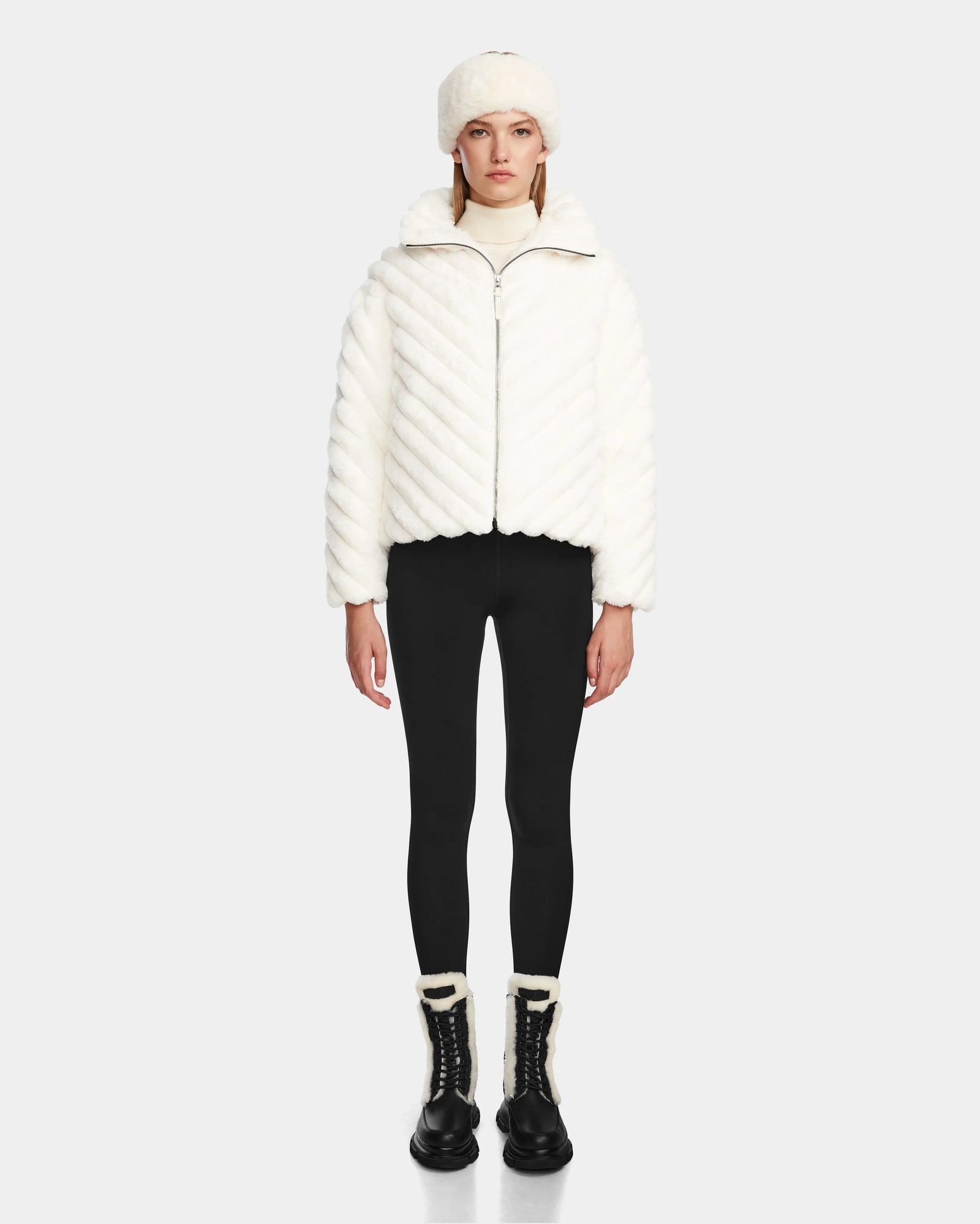 A woman in a white coat and black pants elevates her style with the Rudsak ANASTASIA - 8124804 Iceland, an RDS-certified down womens puffer that seamlessly balances warmth and sophistication.