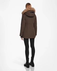A person with straight, shoulder-length hair stands with their back to the camera wearing the Rudsak AURORE - L123561 Espresso women’s down parka with faux fur trim, black leggings, and black boots against a white background.