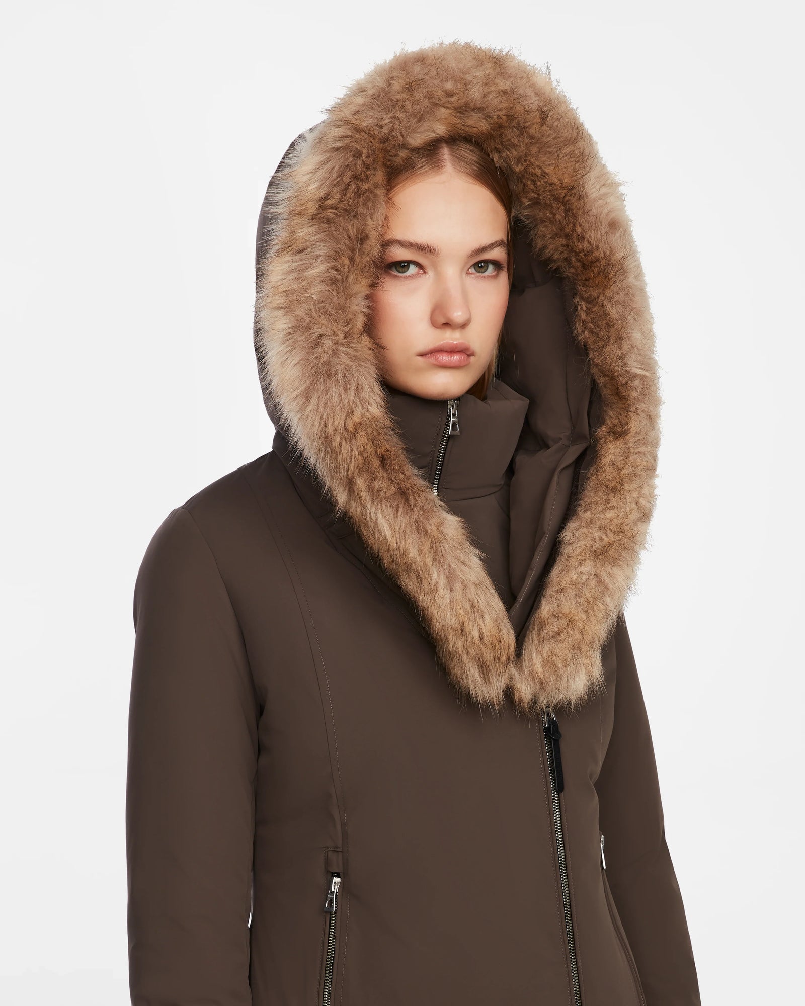 A person wearing the Rudsak AURORE - L123561 Espresso fitted winter parka with a large fur-lined hood looks directly at the camera, expression neutral, set against a plain white background.