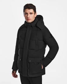 A man with short brown hair wears the Rudsak CARLOS - M124509 Black quilted parka with a hood and front pockets, standing against a plain white background.