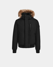 The DEACON - M123513 Black/Natural by Rudsak is a black bomber-style down puffer featuring a high collar, front zipper, ribbed cuffs and hem, detachable hood with brown faux fur trim, and recycled leather accents, shown on a plain white background.