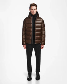 A person stands facing forward, wearing the Rudsak DEMIAN S - M123508 Espresso mens down puffer over a black turtleneck, black pants, and black boots, against a plain white background.