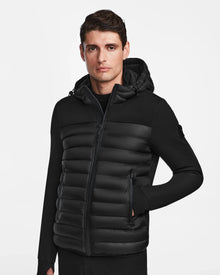 A man wears the Rudsak DURIN M - M123515 Black men’s hooded jacket with waterproof zippers and lightweight down insulation, standing against a plain white background and looking at the camera with a neutral expression.