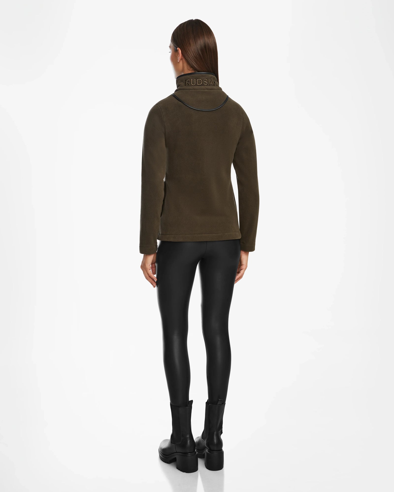 A woman faces away in the EDITH - 8524617 Army jacket by Rudsak, styled with black faux leather leggings and ankle boots for an effortlessly chic look against a crisp white background.