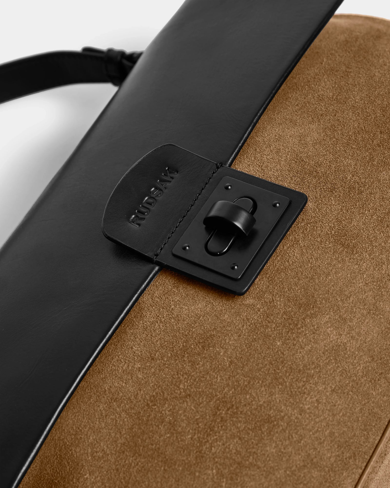 Close-up of the Rudsak ESMA - 8324519 Camel handbag, featuring suede leather with a black flap, matte clasp, embossed branding near the clasp, and a removable shoulder strap for versatile style.