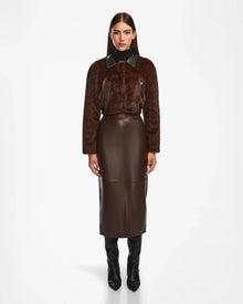 A woman faces forward in a Rudsak EVELYN - 8124791 Espresso dark brown faux fur jacket with a black collar, styled with a high-waisted brown leather midi skirt and knee-high black boots against a plain white background.