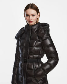 A woman with straight brown hair models the Rudsak FRIDA L-S - L124525 Black belted puffer coat with a hood, standing against a plain white background—an ideal addition to any winter wardrobe.