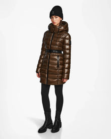 A person wearing the Rudsak FRIDA S - L123513 women's mid-length down jacket in light olive, styled with black leggings, black ankle boots, and a black beanie stands against a plain white background.
