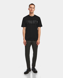 A man faces forward wearing the Rudsak GIANNI - 6524535 Black mens t-shirt, paired with dark fitted pants and black shoes, standing against a plain white background for a modern look.