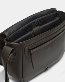 The Rudsak GRAYSON - 8324512 in Espresso is a dark brown leather crossbody bag featuring an adjustable strap, front zip pocket, textured exterior, and black quilted lining, shown open to display its roomy compartments.