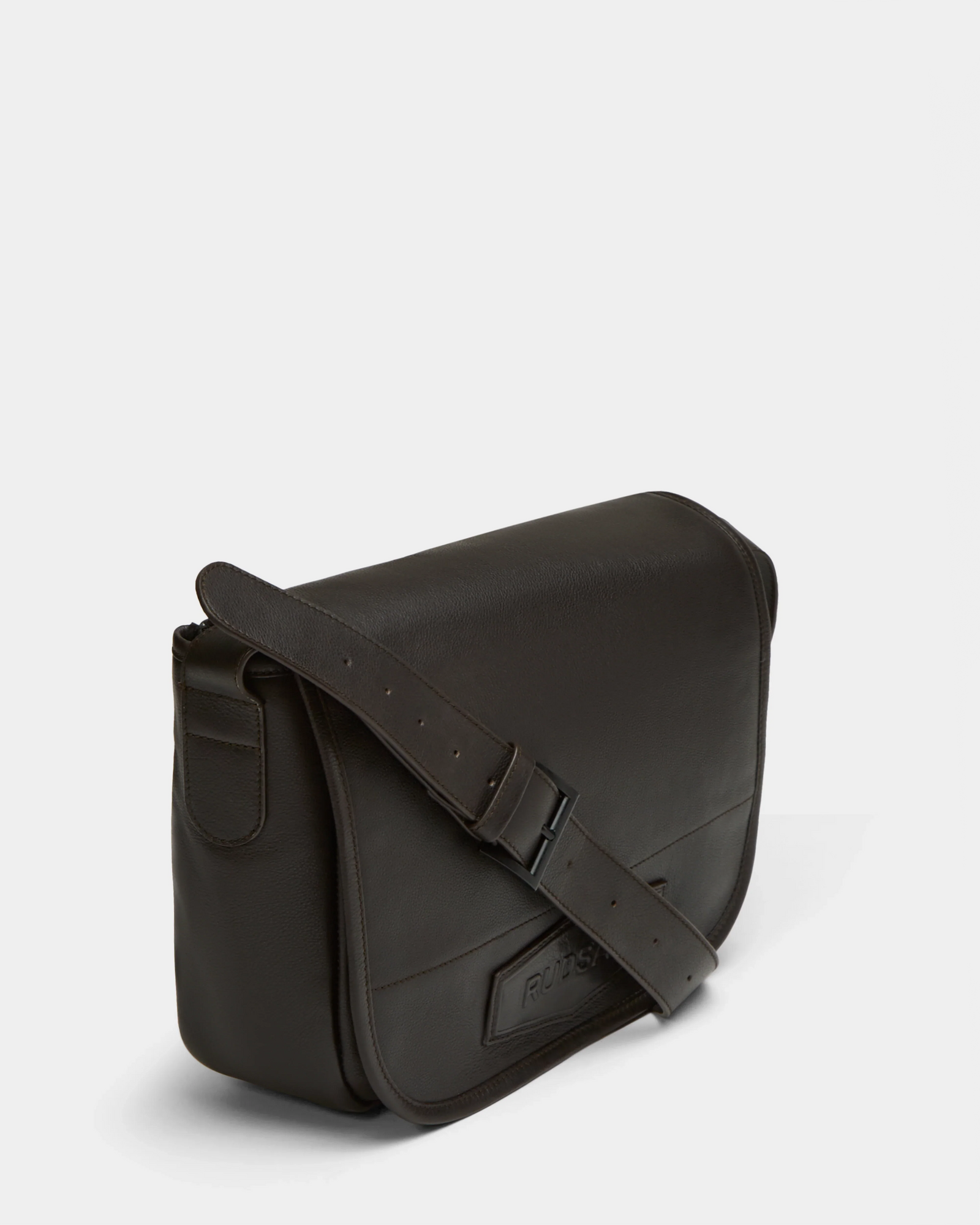 The Rudsak GRAYSON - 8324512 Espresso is a dark brown leather crossbody bag with a front flap, adjustable shoulder strap, and visible stitching, displayed against a plain light background.