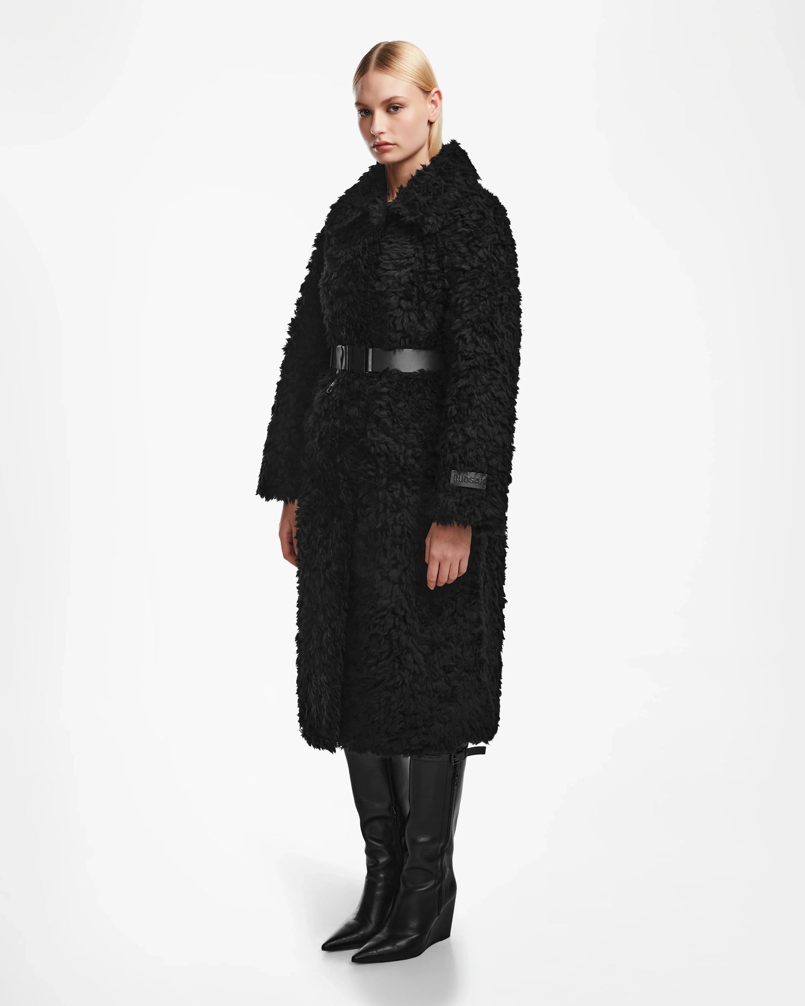 A woman in the Rudsak KAMILAH - 8124827 Black wool teddy coat, styled with a chic vegan leather waist belt.