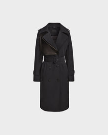 The KINDA - 8124690 Black by Rudsak is a womens long black trench coat with leather accents, double-breasted front, belted waist, wide lapels, and buttoned cuffs, shown on a plain light gray background.