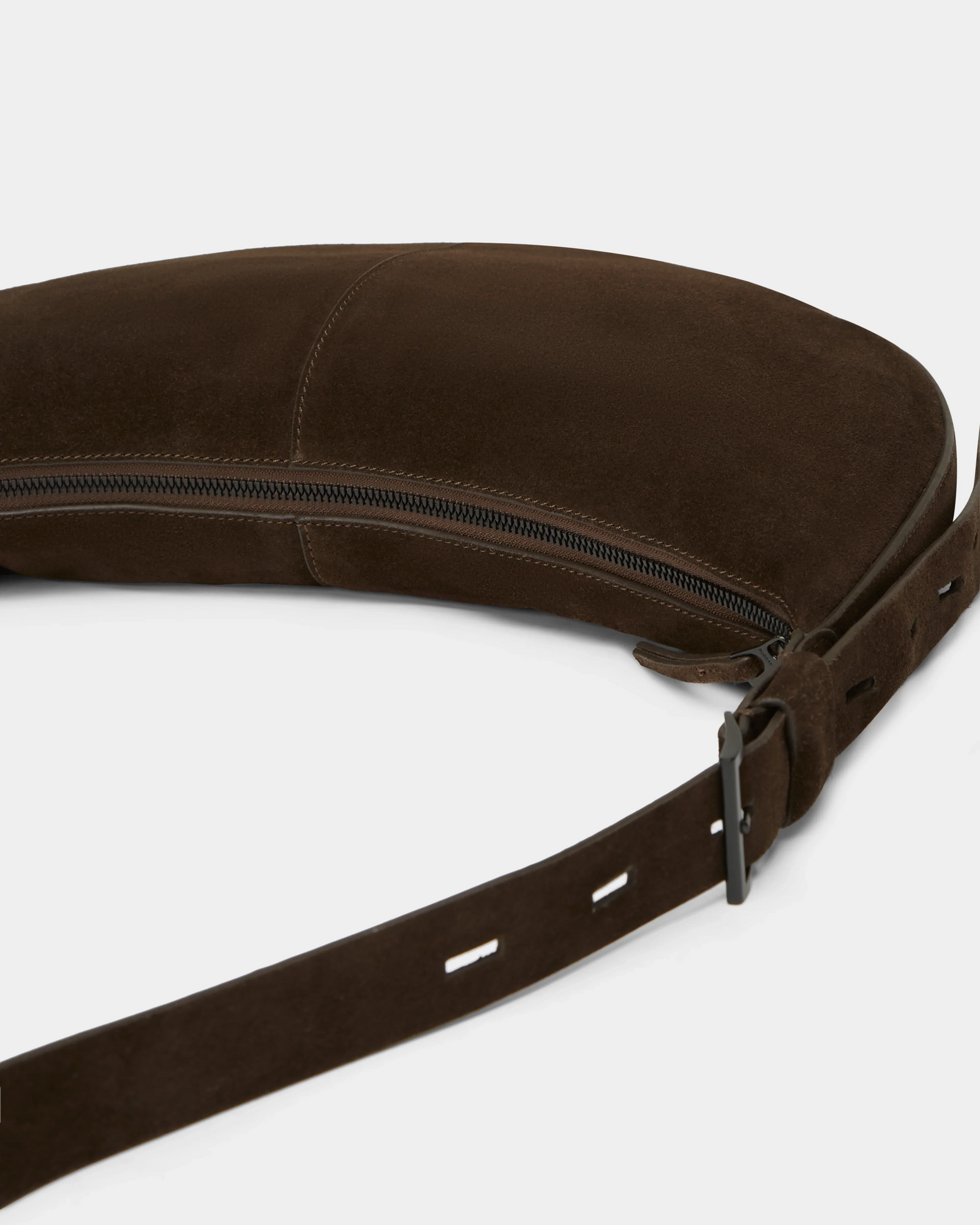 Close-up of the Rudsak LANISSA S - 8324520 Espresso: a dark brown suede crossbody bag with a visible zipper, adjustable punched-hole strap, and metal buckle. Its soft material and minimalist design offer an elegant choice for women.